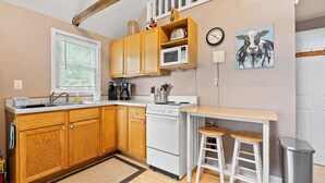 Cocina compacta con armarios de madera, microondas, estufa y pileta.