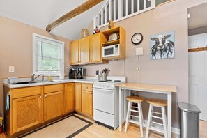 A compact kitchen with wooden cabinets, a microwave, a stove, and a sink. - Tiger Lily Cabin: Sunset Shores Kangaroo Lakefront (Baileys Harbor)