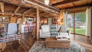 Interior rústico de una cabaña con comedor, cocina y zona de estar con vistas al exterior.