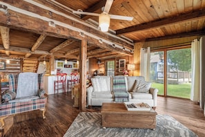A rustic cabin interior with a dining area, kitchen, and seating with a view of the outdoors.
