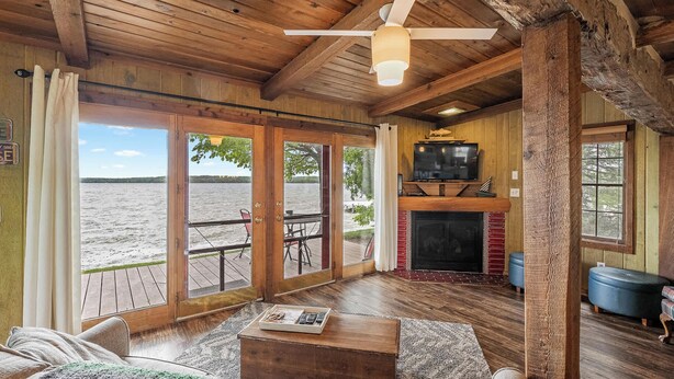 Una cabaña con interior de madera, chimenea, televisión y vista al agua.
