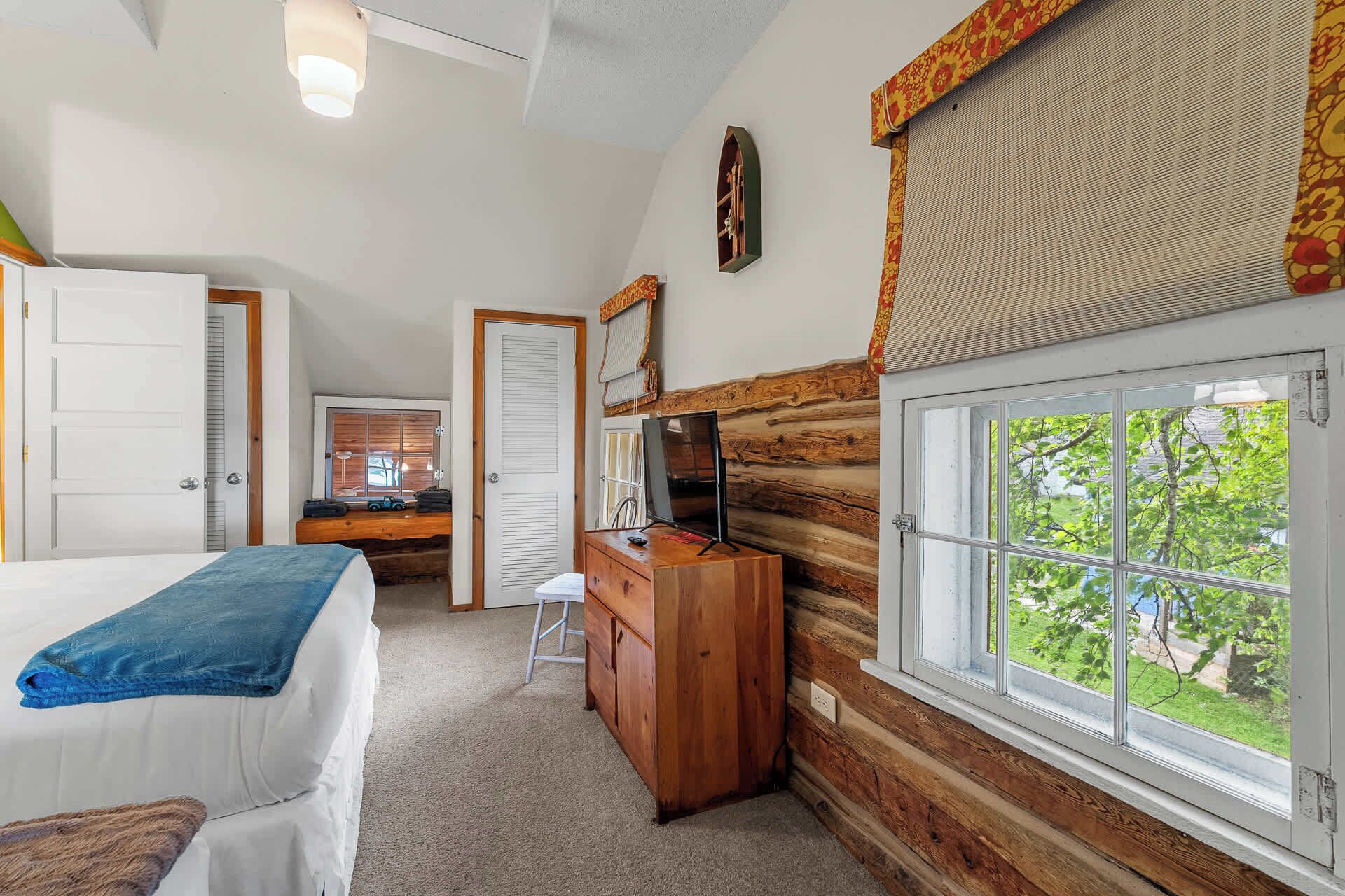 Une chambre à coucher comprenant un lit, une commode, un bureau, une fenêtre donnant sur un paysage agréable et une porte.