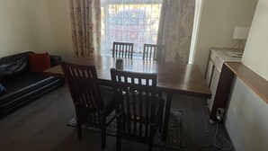 A dining area with a table and chairs, a sofa, a lamp, and a window with curtains. - Immaculate 3-bed House in Luton (Luton)