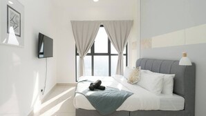 Een moderne slaapkamer met een groot bed, een flatscreen televisie en een uitzicht over de stad door een groot raam.