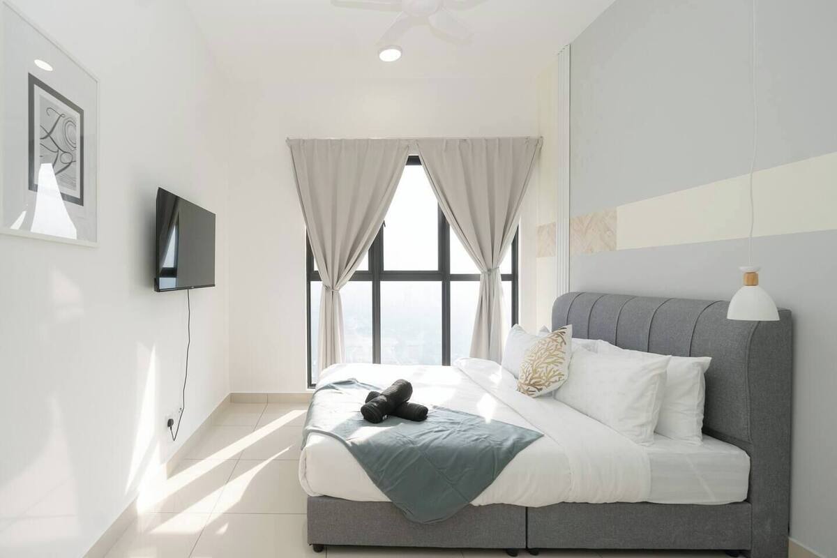 A modern bedroom with a large bed, a flat-screen TV, and a view of the city through a large window.