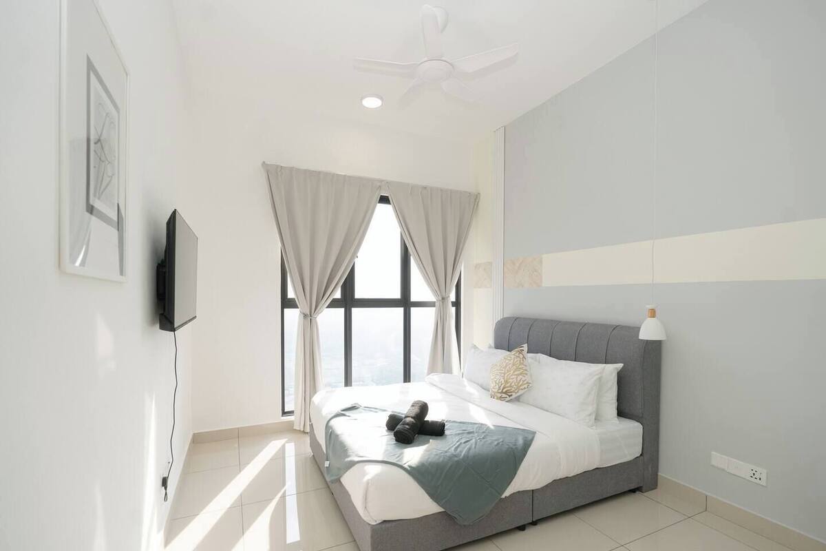 A modern bedroom with a bed, curtains, a ceiling fan, and a TV mounted on the wall.