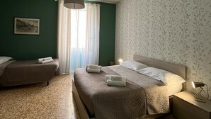 A hotel room with a bed, a bedside table, a lamp, a window with curtains, and a wall with a floral pattern. - Family-friendly apartment near the port and train station (Civitavecchia)