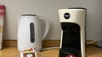 Två kaffemaskiner står på en träyta, och framför varje maskin finns en korg med kaffekapslar.