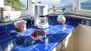 A kitchen with a coffee maker, a jar of nuts, and a bowl of berries on a blue-tiled counter. - Villa Grazielluccia with Sea View and Pool (Priora)