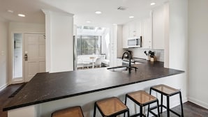 Une cuisine moderne dotée d’un plan de travail en granit foncé, de meubles blancs et d’un îlot central avec des tabourets de bar.