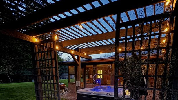 Un espacio al aire libre techado con un jacuzzi, una pérgola de madera y vistas a un edificio con grandes ventanales.