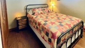 Una cama individual en una habitación con suelo de madera, dos ventanas y una lámpara de noche.
