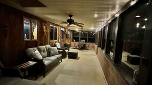 Un espacio de estar al aire libre con techo, varios sofás y sillones, ventiladores de techo y ventanas amplias.
