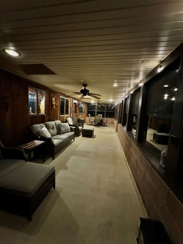 A covered outdoor seating area with multiple sofas and chairs, ceiling fans, and large windows. - Secluded house built into the earth. Pet friendly, fishing, hot tub, Wi-Fi! (Magnolia)
