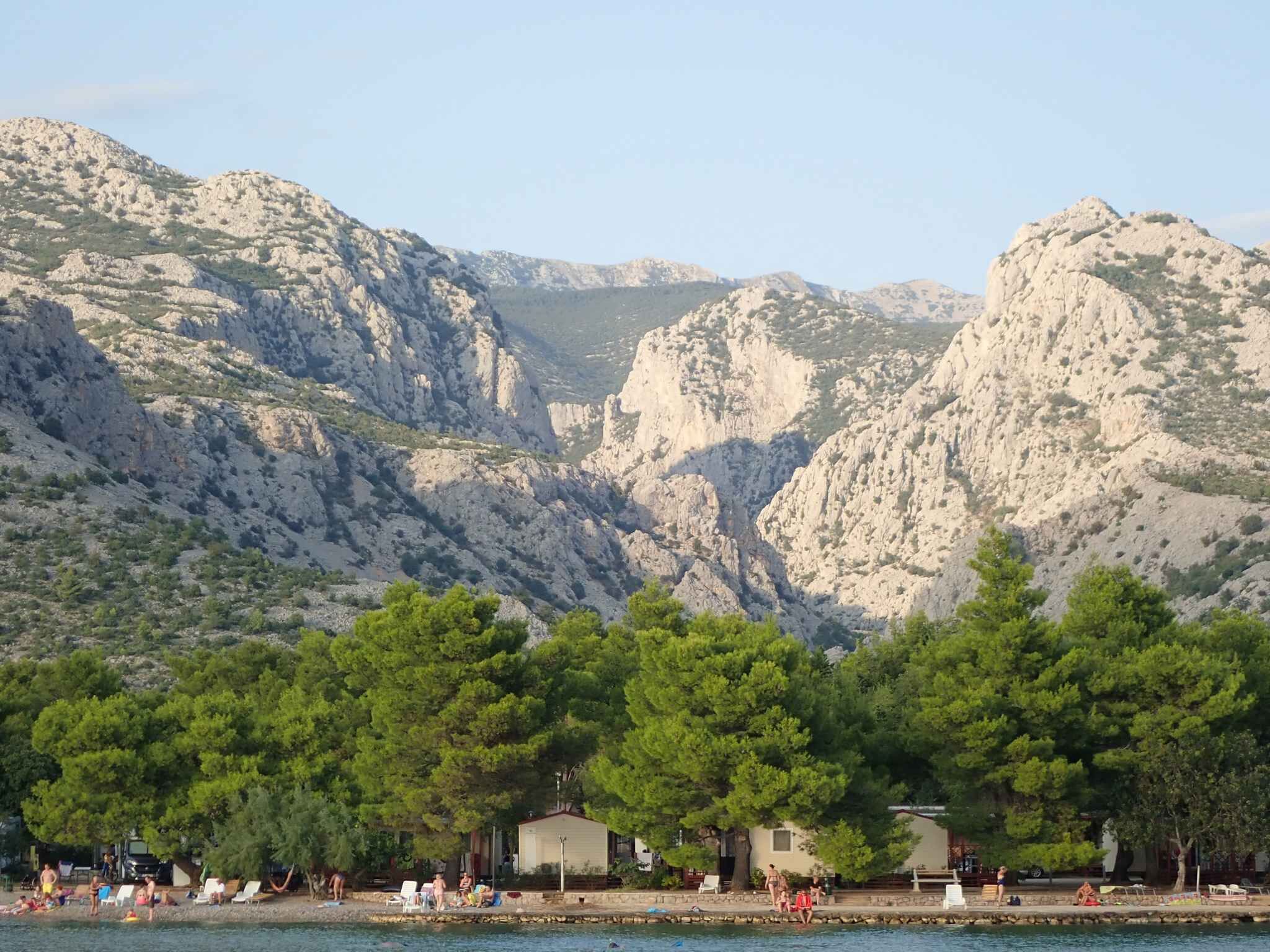 Zona costera con montañas rocosas al fondo, una playa con árboles y varias construcciones que probablemente son alojamientos.