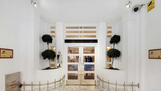 A hotel lobby with a marble floor, a reception desk, and two potted trees. - The Princes Residences (London)