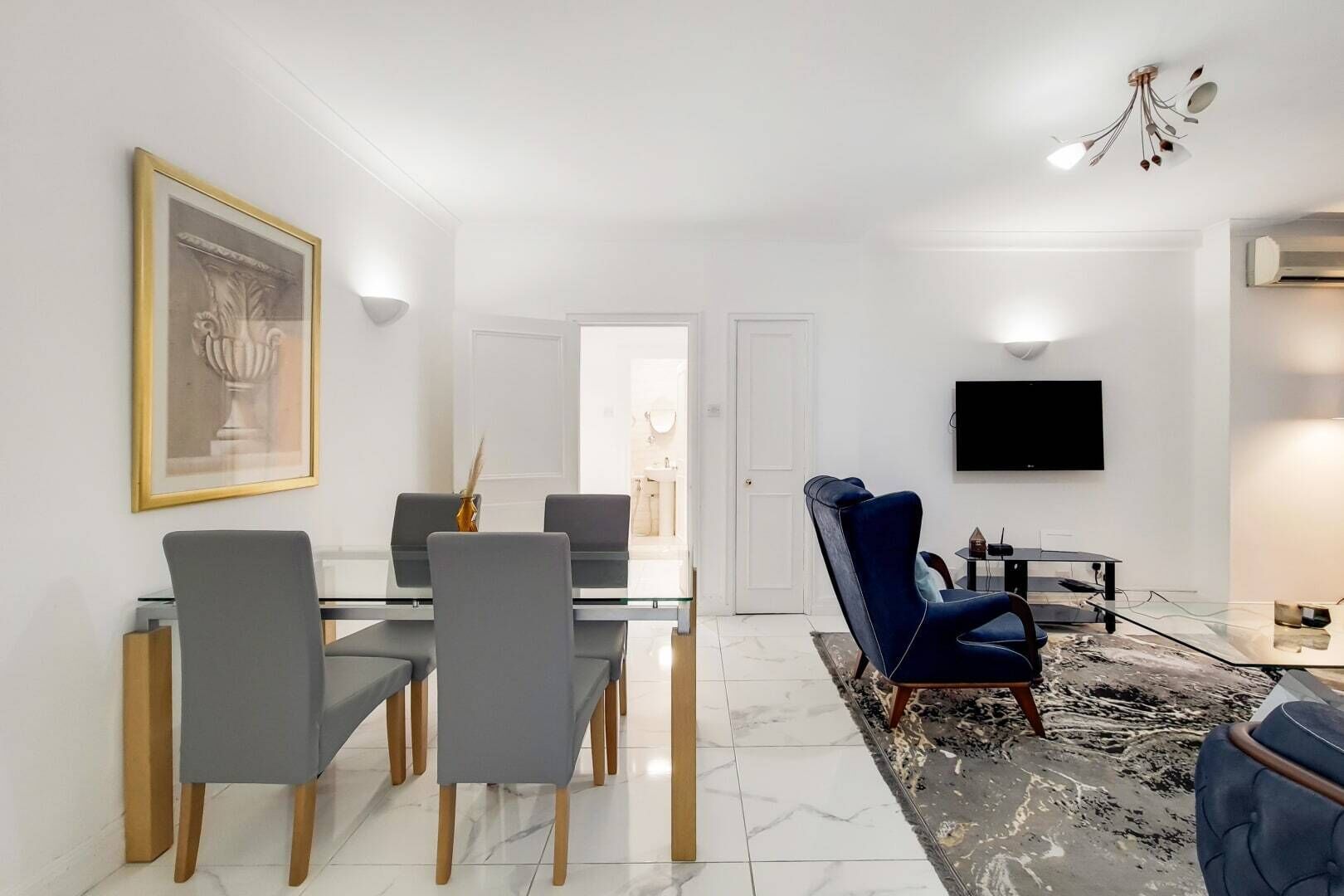 Een moderne eetruimte met een glazen tafel, grijze stoelen en een blauwe bank.