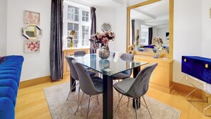 A modern dining area with a glass table, grey chairs, and a blue sofa. - The Princes Residences (London)