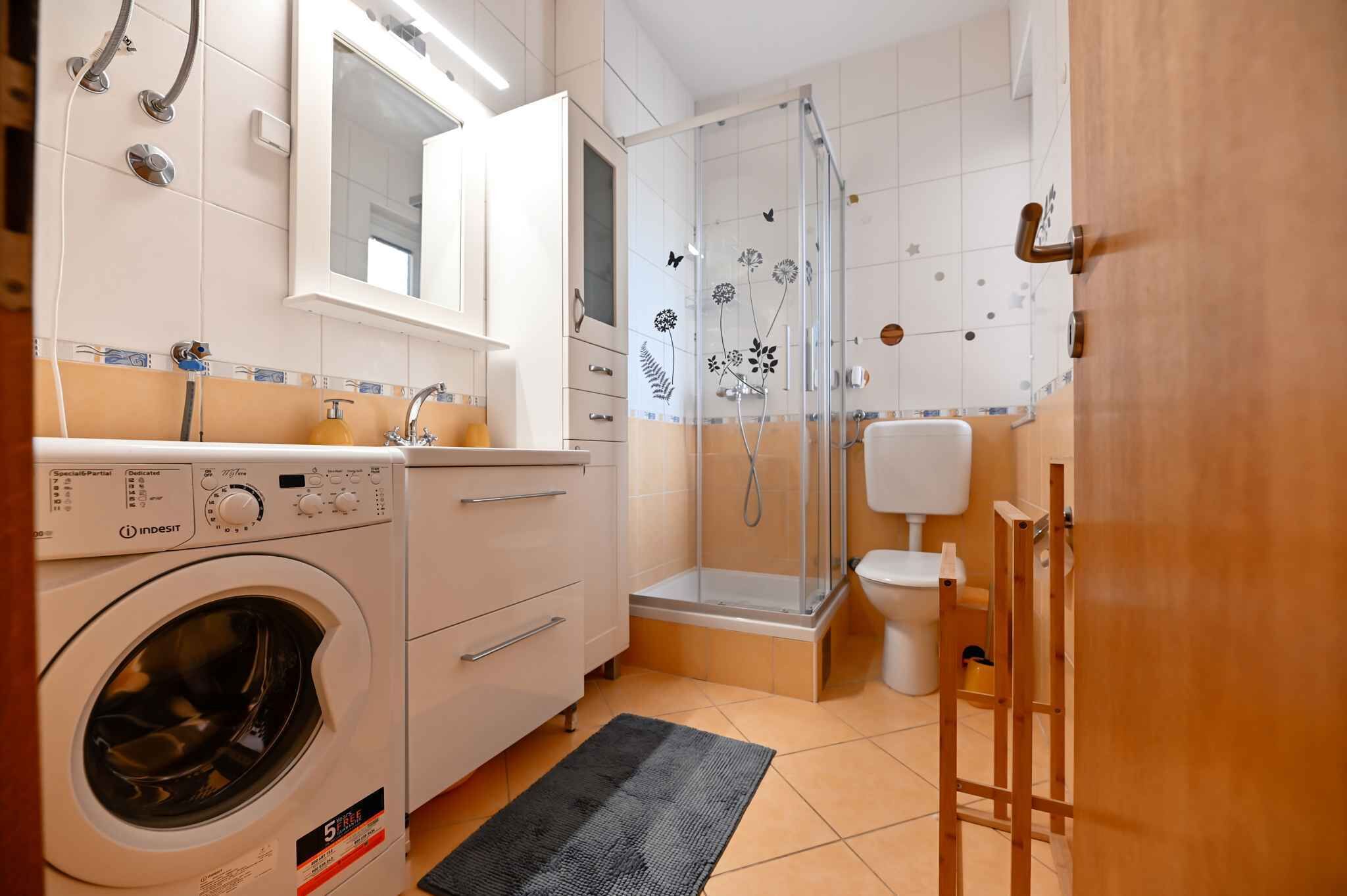 Ein kleines Badezimmer mit Waschmaschine, Duschkabine und Toilette.