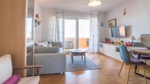 A modern living room with a sofa, a dining table with chairs, a small round table, and a TV mounted on the wall. - Holiday apartment with balcony and partial sea view (Biograd na Moru)