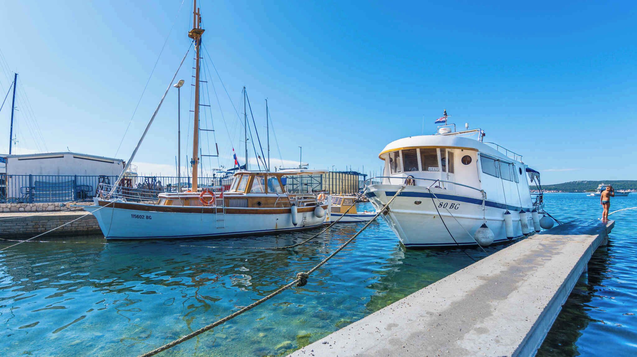 Un puerto deportivo con dos barcos amarrados, un edificio de fachada blanca y un cielo azul despejado.