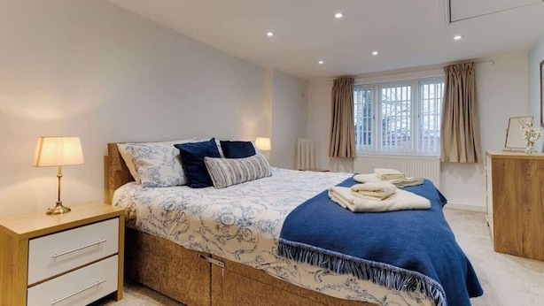 A bedroom with a bed, bedside table, lamp, window with curtains, and a wooden dresser. - Cosy one bedroom cottage in Pickering (Pickering)