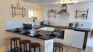 A modern kitchen with a central island, bar stools, a microwave, and a built-in oven. - Lavender Cottage - a beautiful quirky cottage (Snainton)