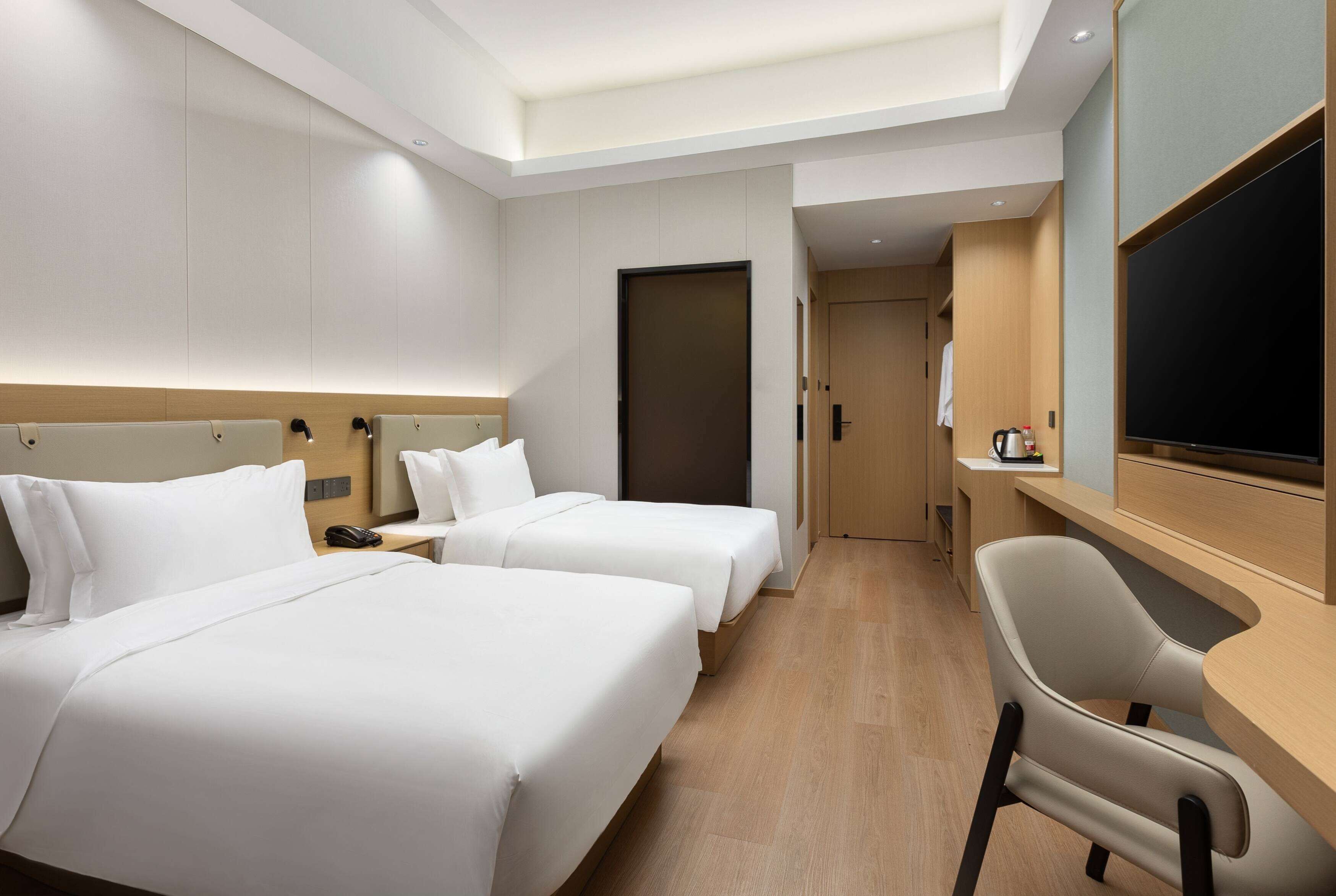 A hotel room with two beds, a desk, a chair, a television, and a door leading to a bathroom.