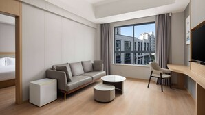 Una habitación de hotel moderna con un sofá, una mesita, una silla, un televisor y una ventana con vistas a la ciudad.