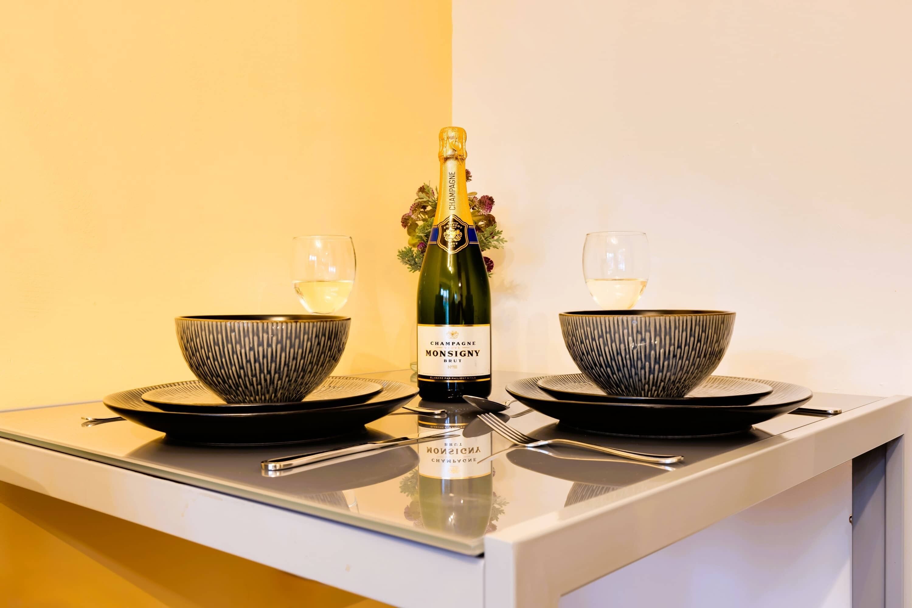 A table with a bottle of champagne, two bowls, and two glasses.