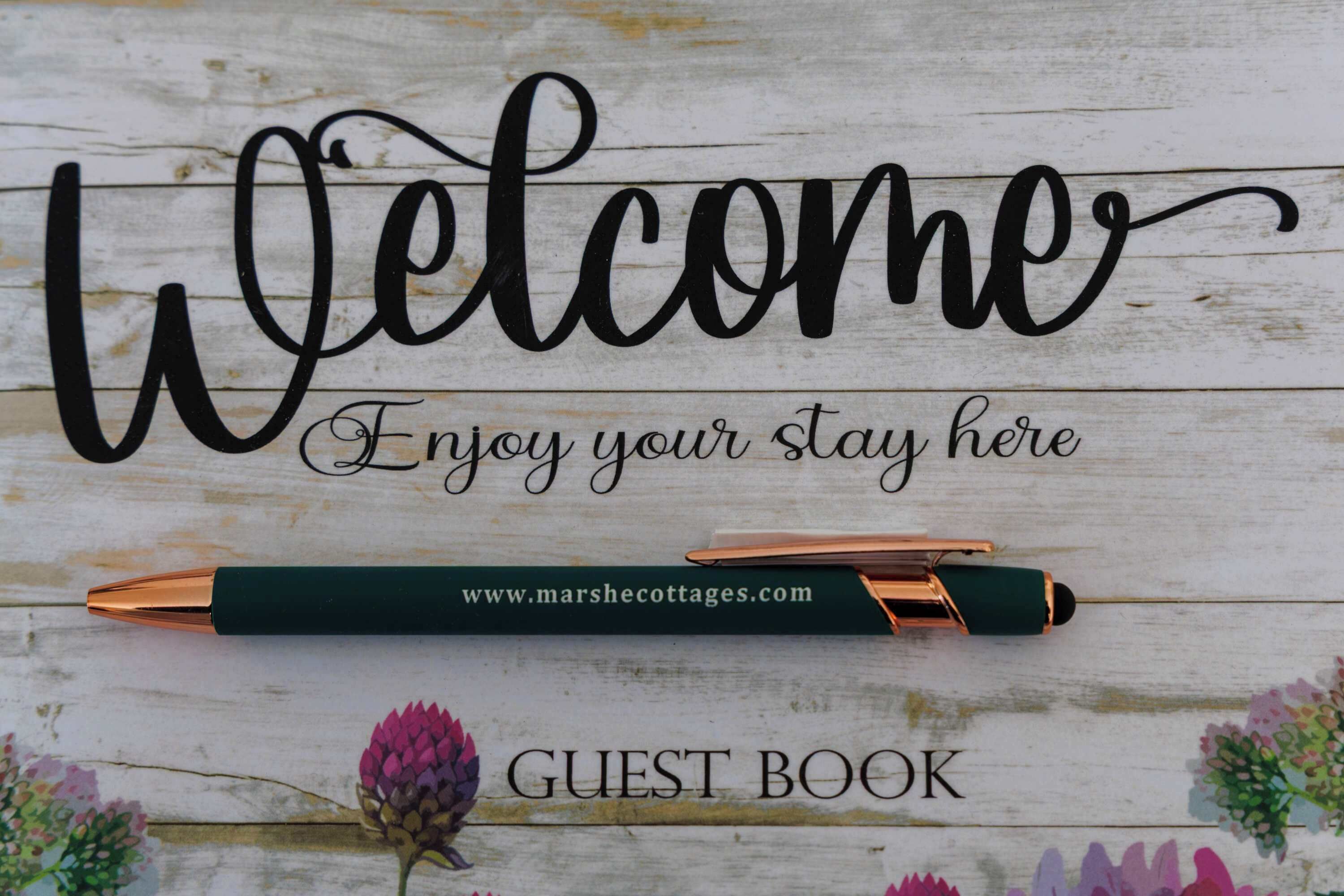 Un cartello con la scritta 'Welcome', una penna e l'etichetta 'Guest Book' su una superficie in legno.