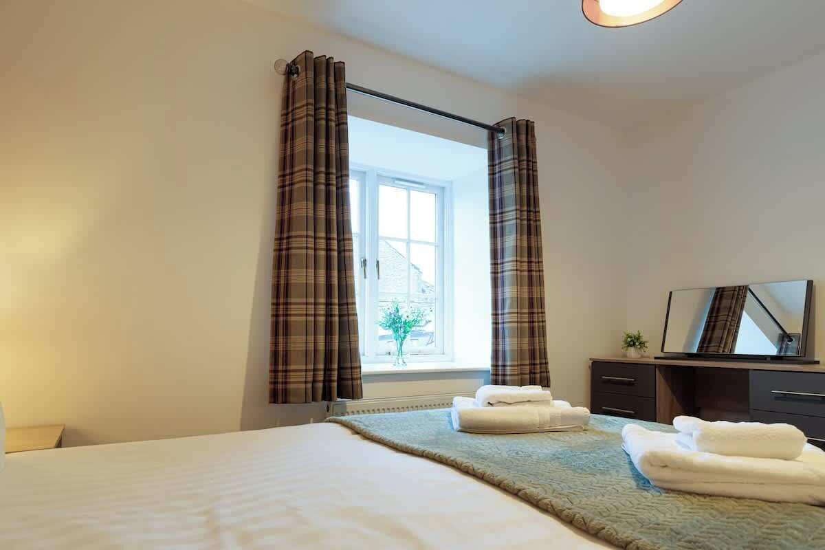 Ein Hotelzimmer mit Bett, einem Vorhangfenster, einem Schreibtisch mit Spiegel und Handtüchern auf dem Bett.