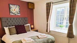 A neatly made bed with a green quilt, a headboard, a bedside table with a lamp, and a window with curtains. - Heather Cottage - a beautiful cosy cottage (Snainton)