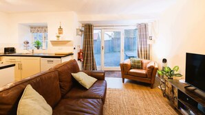 A living room with a brown leather sofa, a television, and a kitchen area with a toaster and a plant. - Heather Cottage - a beautiful cosy cottage (Snainton)