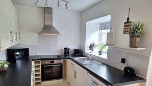 A compact kitchen with white cabinets, a black countertop, a microwave, a coffee maker, and a sink. - Heather Cottage - a beautiful cosy cottage (Snainton)