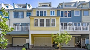 Une rangée de maisons de ville avec des garages attenants, un petit arbre dans le jardin avant et un ciel bleu dégagé.