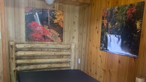 Ein Zimmer in einer Holzhütte mit einem Bett, Holzwänden und einem Bild eines Wasserfalls.