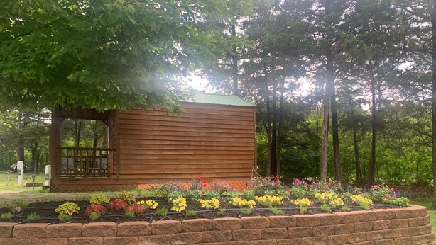 Eine kleine Holzhütte mit einer Veranda, umgeben von einem Blumenbeet mit bunten Blumen.