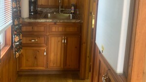 Eine kleine Küche mit Holzausstattung, einer Mikrowelle, einem Kühlschrank, einer Kaffeemaschine und einem Spülbecken.