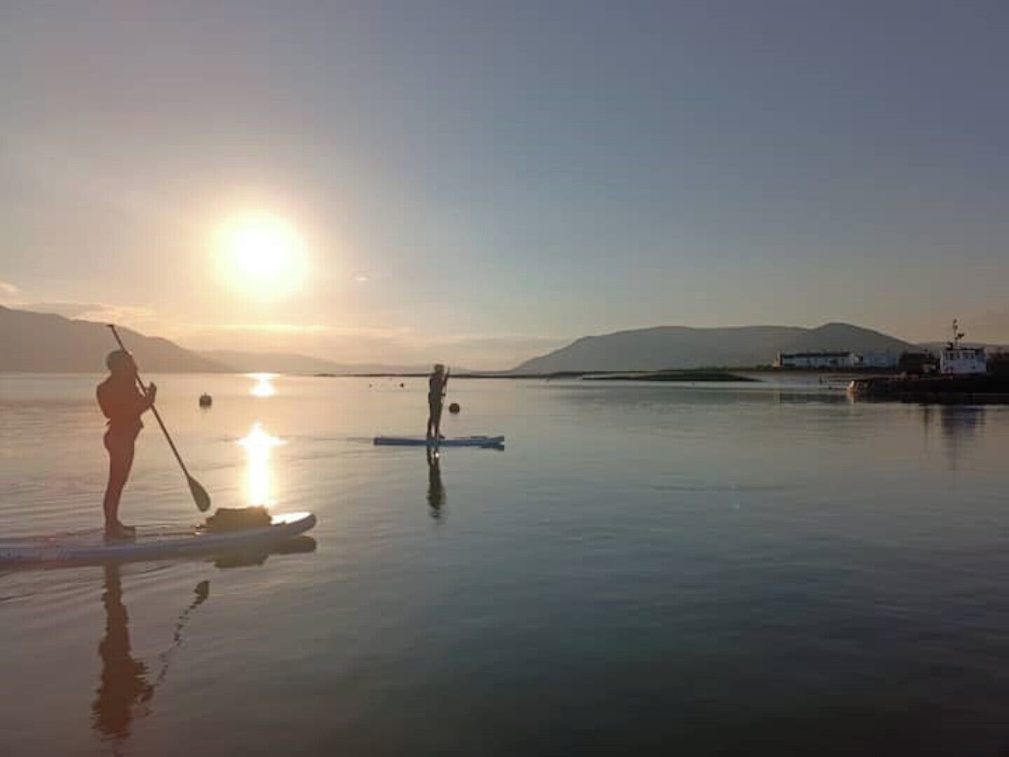 Une personne pratiquant le stand-up paddle sur une eau calme, au lever ou au coucher du soleil.