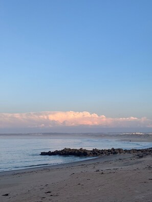A beach with a rocky breakwater and a distant shoreline with buildings. - Go4surf Beachlofts (Peniche)