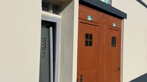A building with a white exterior, a wooden door with a window, and a small sign above the door. - Go4surf Beachlofts (Peniche)