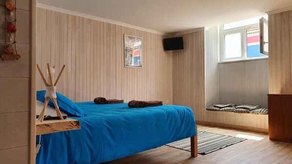 A bedroom with a bed, a TV, a window, and a wooden wall. - Go4surf Beachlofts (Peniche)