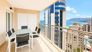 A balcony with a glass table and chairs, overlooking a coastal cityscape with buildings and a clear blue sky. - Alq 292 Porto Azul 14 (Calpe / Calp)