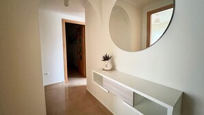 A hallway with a white console table, a round mirror, and a door leading to another room. - Alq 292 Porto Azul 14 (Calpe / Calp)