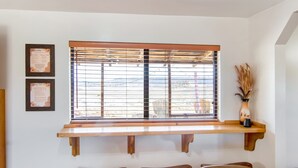 Ein Zimmer mit einem Fenster mit Gitterstäben, einem Holzregal darunter und zwei gerahmten Zertifikaten an der Wand.