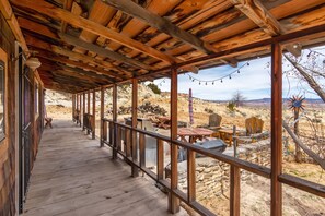 A covered wooden deck with a stone wall and outdoor furniture. - The Desert View Cabin (Monticello)