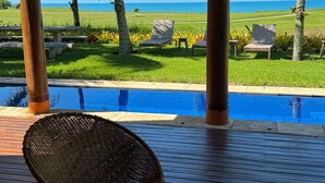 A poolside area with a wicker chair, a small stool, and a view of the ocean and palm trees. - House 4 suites, swimming pool, views of the sea and golf course. Turtle Beach  (Trancoso)