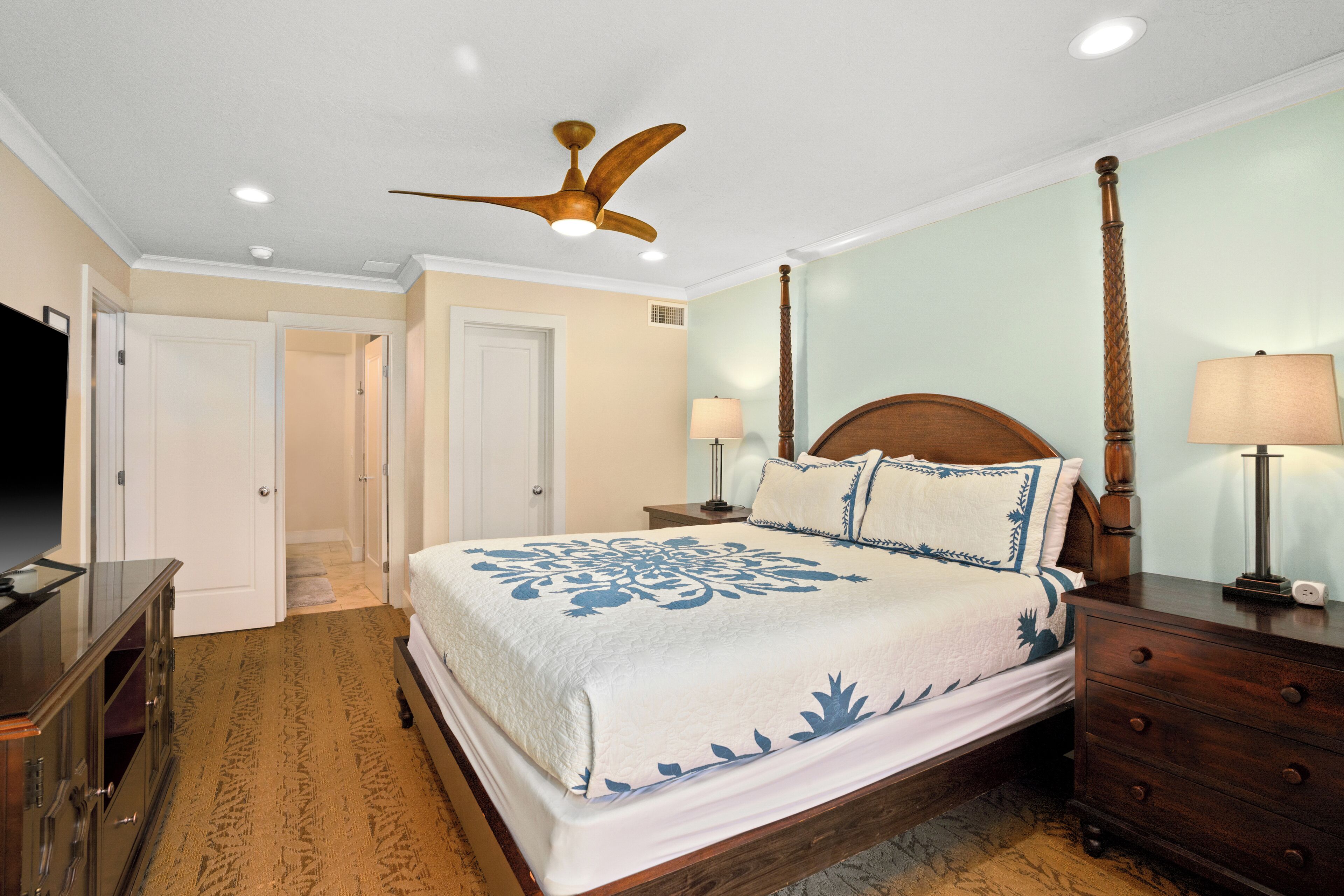 A bedroom with a bed, nightstands, a dresser, a ceiling fan, and a TV.