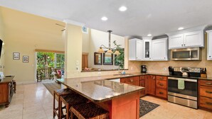 A spacious kitchen with a large island, wooden bar stools, white cabinets, stainless steel appliances, and a view to a balcony.